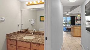 A bathroom with a granite countertop sink, wooden cabinets, and a large mirror with lights above. - 🌅 Gulf Gate Resort Unit 208 – Dual-Balcony Water View Condo for Up to 4 Guests (St Pete Beach)