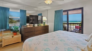 A hotel room with a bed, a dresser, a television, a ceiling fan, and a balcony with a view of the ocean. - 🌅 Gulf Gate Resort Unit 208 – Dual-Balcony Water View Condo for Up to 4 Guests (St Pete Beach)