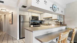 A modern kitchen with a central island, stainless steel appliances, and a large clock on the wall. - 🌿 Unit 107 at Gulf Gate – Peaceful Garden View Comfort for Up to 4 Guests (St Pete Beach)