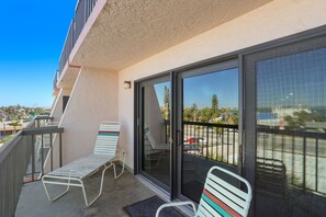 Enjoy the view from this balcony with a glass door leading to an outdoor space, featuring two lounge chairs and a metal railing.