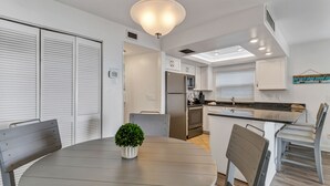 Eine moderne Küche mit weißen Schränken, einem Edelstahlkühlschrank und einem Essbereich mit rundem Tisch und Stühlen.
