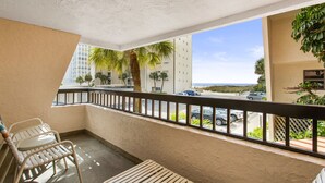 Un balcon avec vue sur la rue et l’océan. On y trouve deux chaises blanches et un banc en bois.