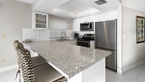 Cozinha moderna com armários brancos, bancada de granito, eletrodomésticos de aço inoxidável e micro-ondas embutido.