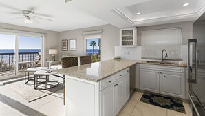 Cozinha moderna com uma ilha grande, armários brancos e vista para o oceano.