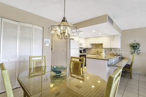 A modern kitchen with white cabinets, a central island, and a dining area with a glass table and wicker chairs.