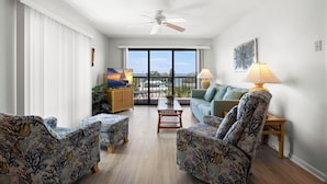 A living room with a ceiling fan, a sofa, two armchairs, a coffee table, and a view through large windows. - !!!Newly Updated, Throughout!!! Gulf Gate 305 | Bay View Family Escape (St Pete Beach)