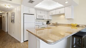 A modern kitchen with white cabinetry, a granite countertop, and a built-in microwave.