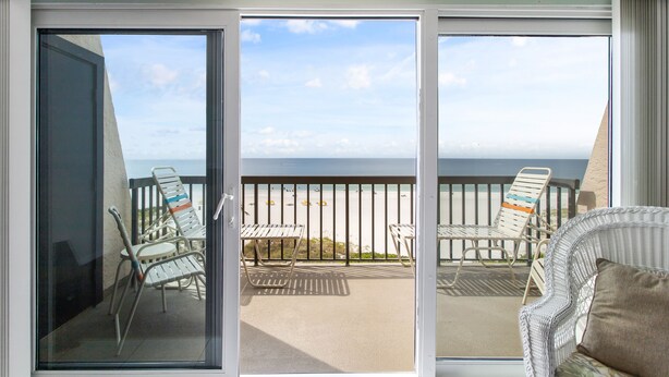 A balcony with a view of the beach, featuring two lounge chairs and a wicker sofa. - Gulf Gate Resort #503 Gulf Front  Heated Pool (St Pete Beach)
