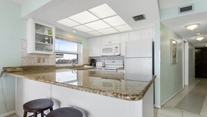 A modern kitchen with a central island, bar stools, white cabinets, and a microwave. - Gulf Gate Resort #503 Gulf Front  Heated Pool (St Pete Beach)