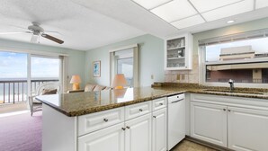 A kitchen with white cabinets, a granite countertop, and a window overlooking the ocean. - Gulf Gate Resort #503 Gulf Front  Heated Pool (St Pete Beach)