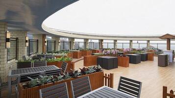 A rooftop lounge with outdoor seating, a bar area, and a view of the city skyline.