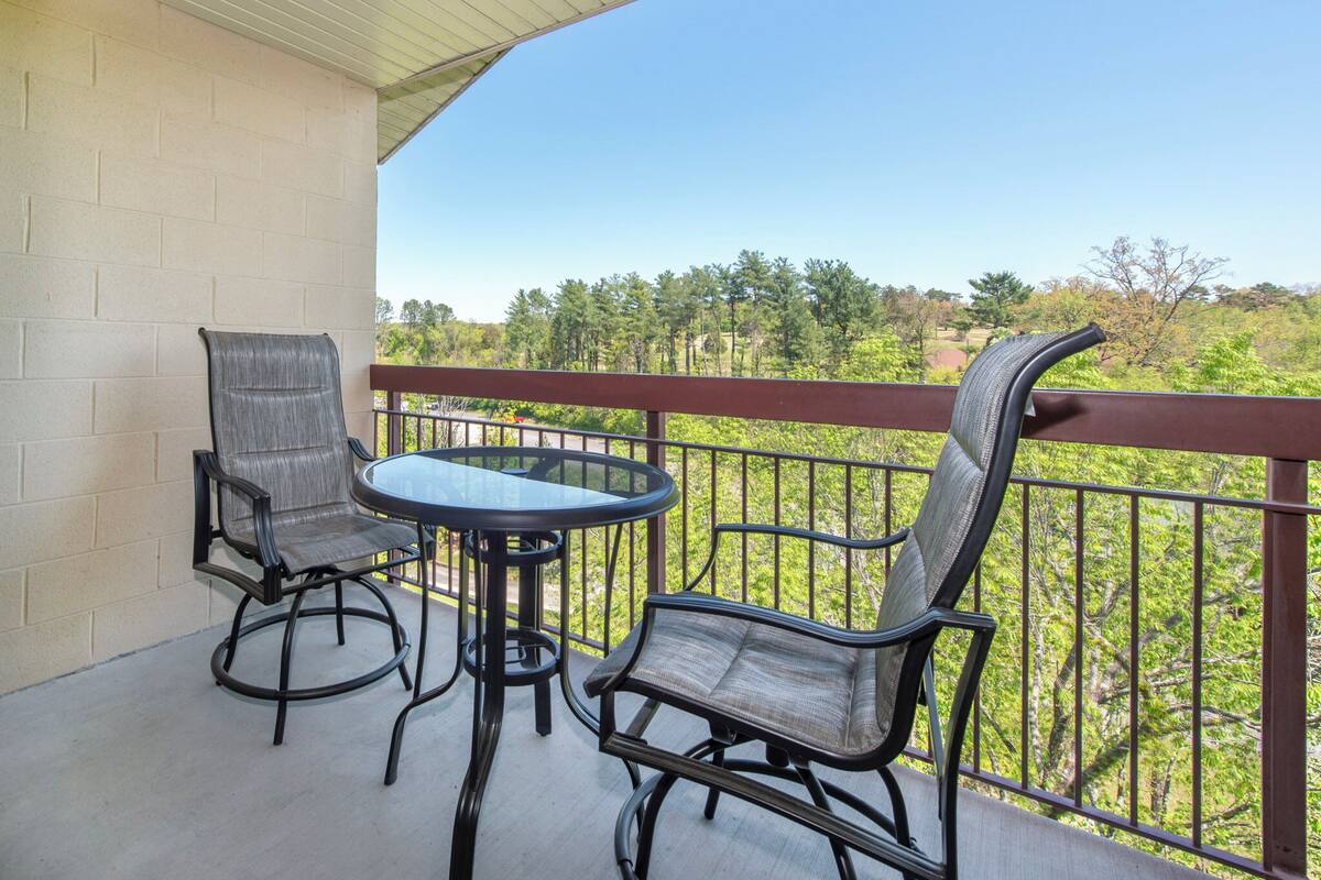 A balcony with two chairs and a table, overlooking a green landscape.