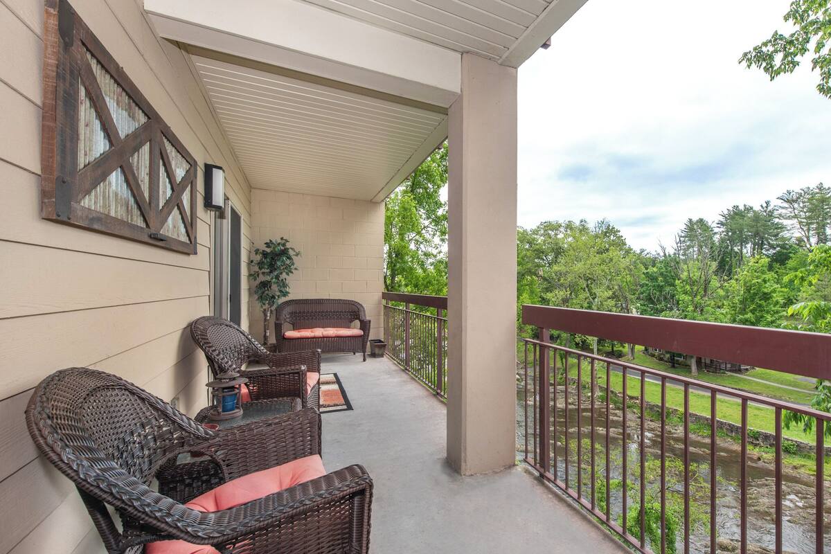 A covered balcony with wicker furniture and a view of a river.