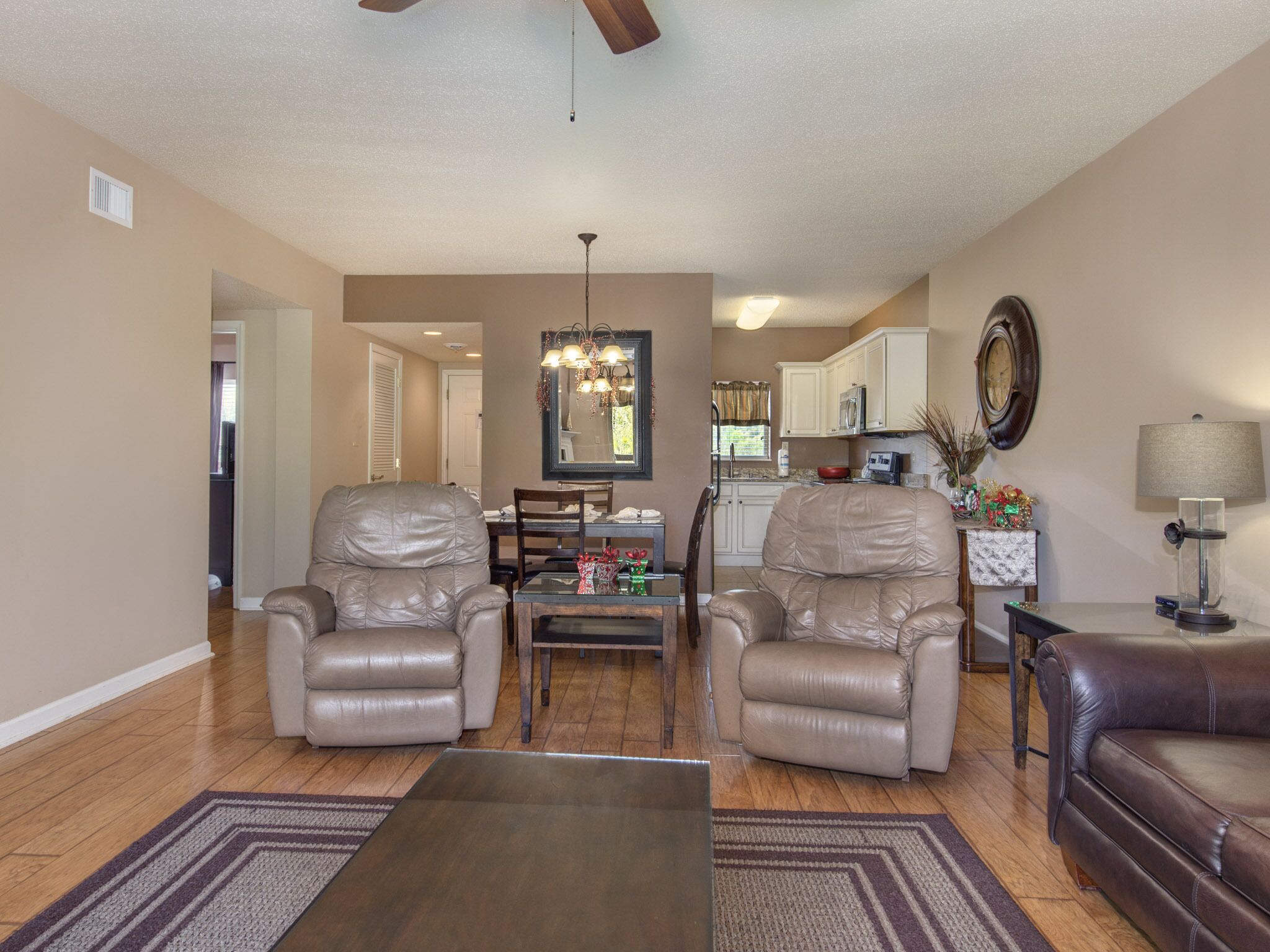 A living room with two leather chairs, a dining table, and a coffee table. There is a kitchen in the background with white cabinets and a microwave.