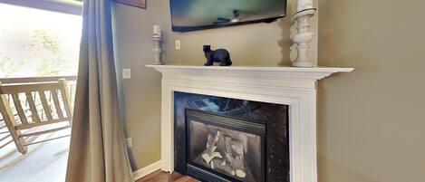 A living room with a fireplace, a mounted TV, and a view of the outdoors.