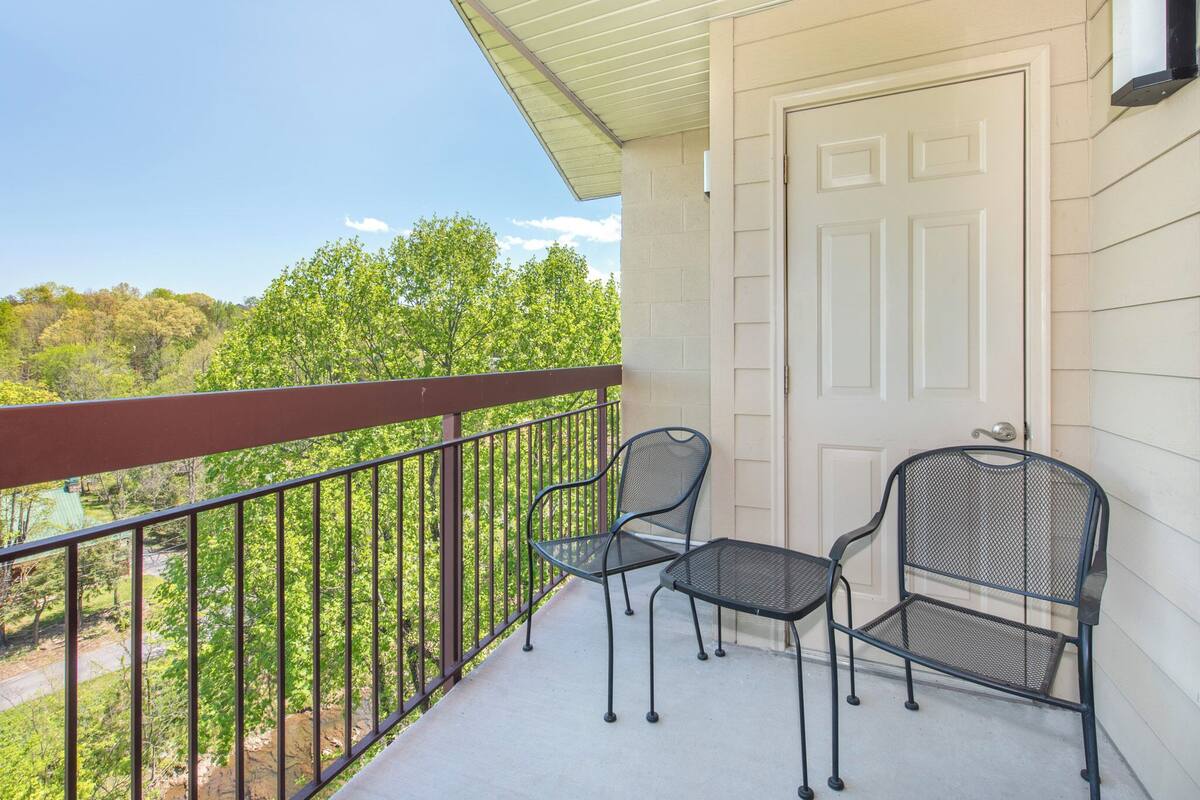 A balcony with a white door, two metal chairs, and a railing overlooking a green landscape.