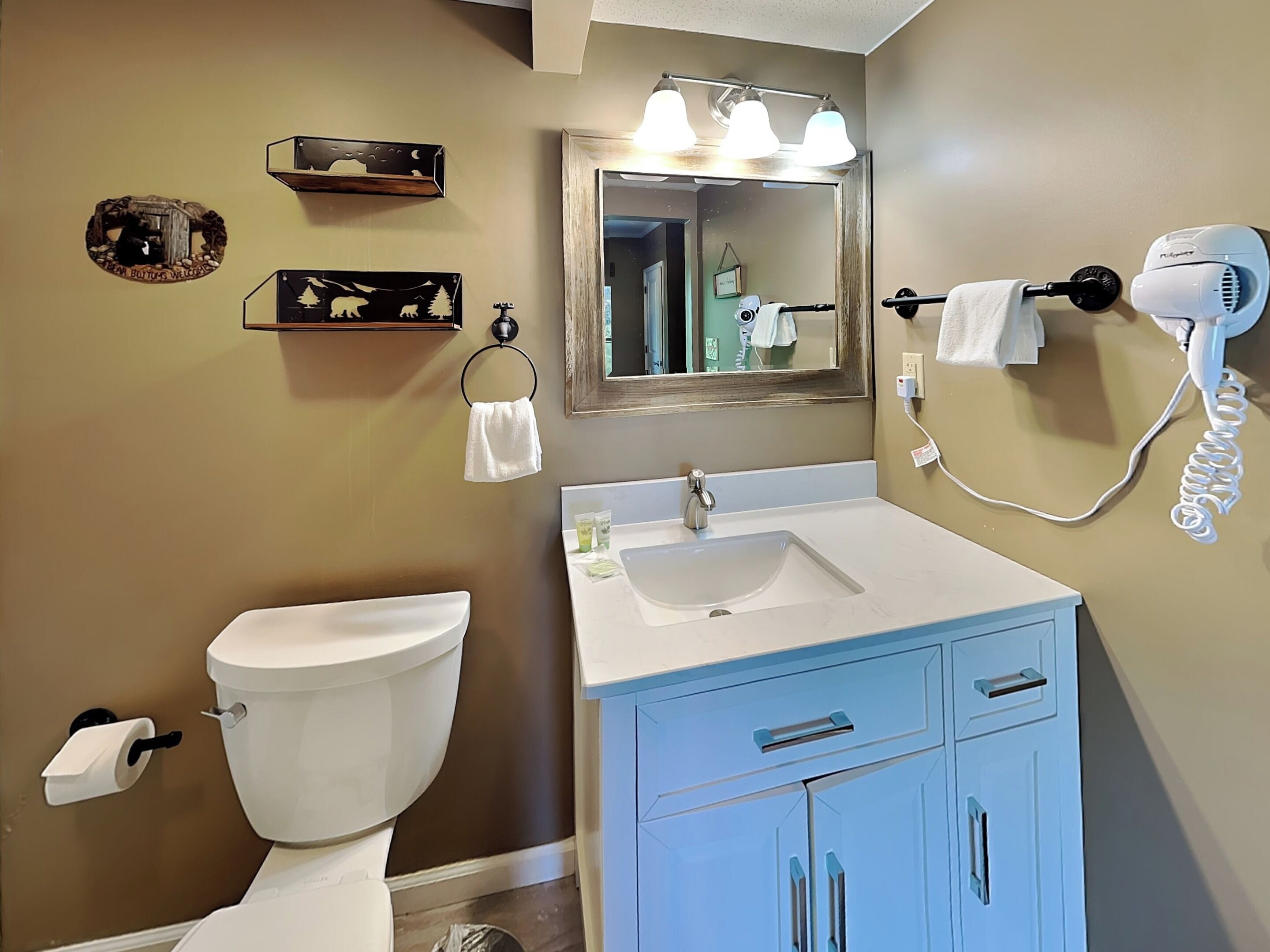 A bathroom with a toilet, sink, vanity, and a hairdryer mounted on the wall.