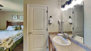 A hotel room with a bed, a bathroom with a sink and mirror, and a door leading to another room.
