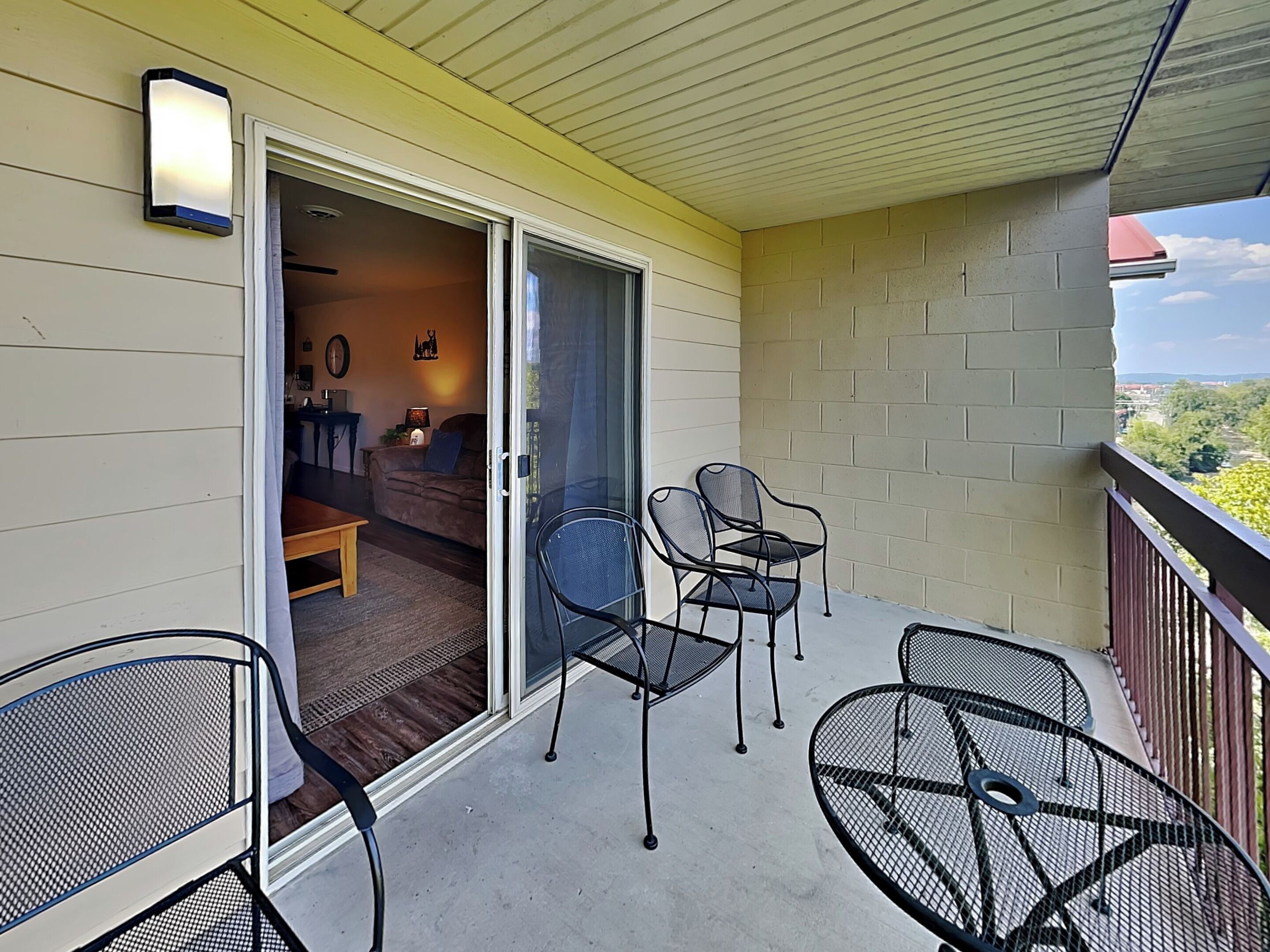A balcony with a sliding glass door leading to a living room, furnished with a sofa, chairs, and a table.