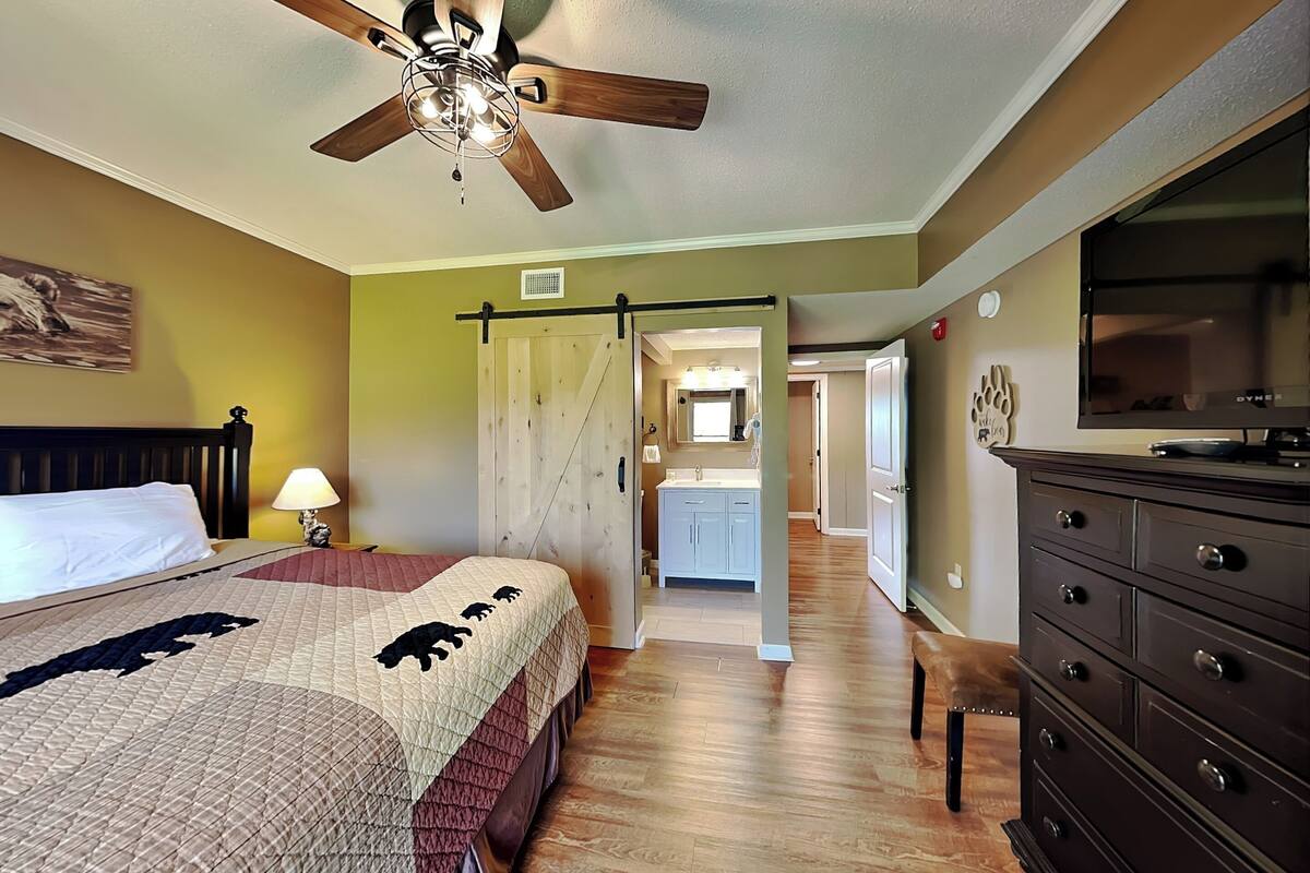 A bedroom with a bed, a dresser, a ceiling fan, and a TV.
