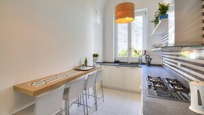 A modern kitchen with a bar area, white cabinets, a gas stove, and a hanging pendant light.