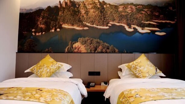 A hotel room with two beds, a large painting of a landscape, and a wooden nightstand. - Fortune Hotel (Taining)