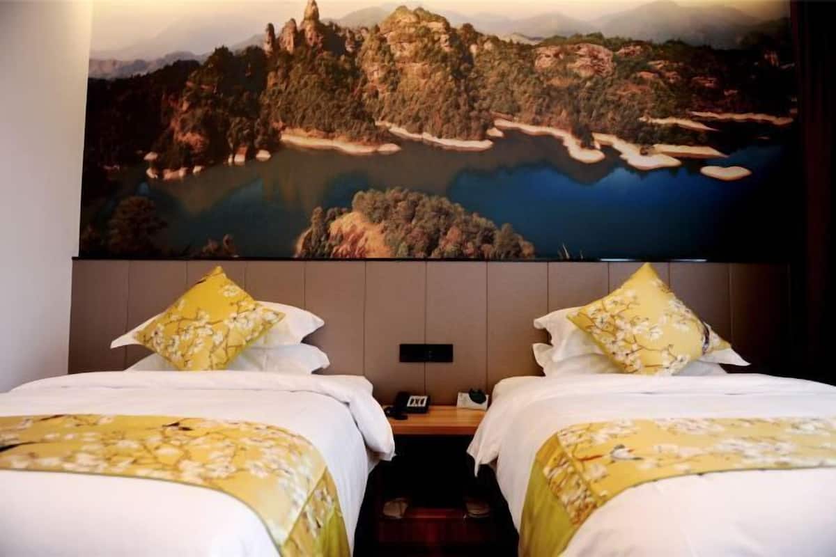 A hotel room with two beds, a large painting of a landscape, and a wooden nightstand.