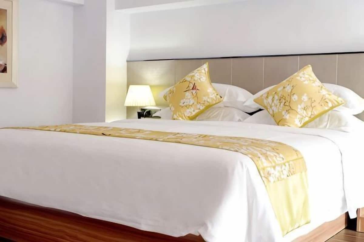 A hotel room with a large bed, two pillows with floral patterns, a bedside lamp, and a wooden headboard.