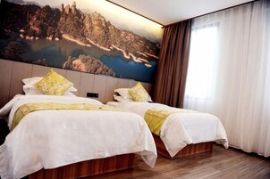 Una habitación de hotel con dos camas, un cuadro grande de un paisaje y una ventana con cortinas.