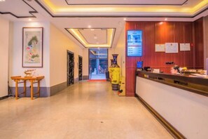 A hotel reception area with a wooden reception desk, a framed artwork on the wall, and a digital screen displaying information. - Fortune Hotel (Taining)