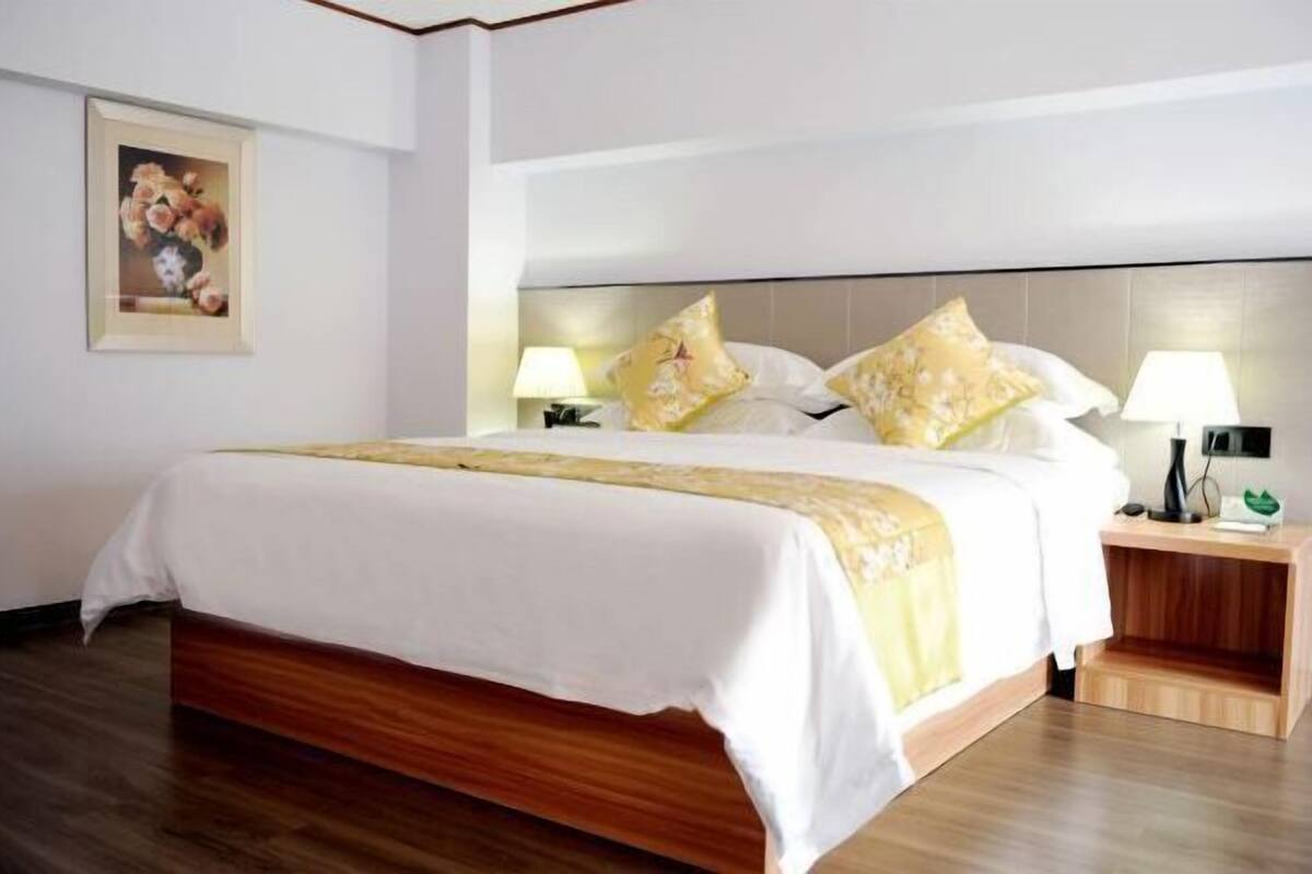 A hotel room with a wooden bed, white bedding, two bedside lamps, and a framed picture on the wall.