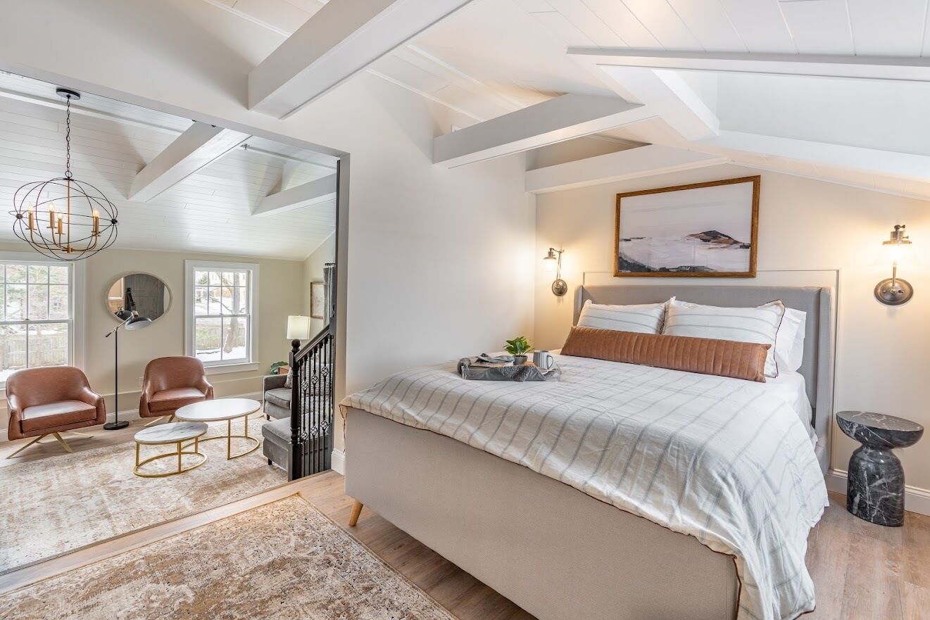Ein Schlafzimmer mit einem großen Bett, zwei Stühlen, einem kleinen Tisch und einer Deckenleuchte.