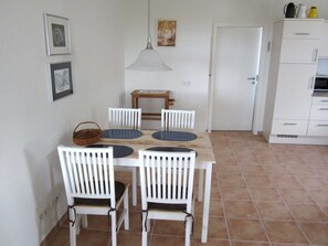 Uma sala de jantar com uma mesa e cadeiras brancas, um lustre pendurado e uma porta ao fundo.