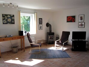 Sala de estar com uma escrivaninha de madeira, duas cadeiras, uma televisão e uma lareira a lenha.