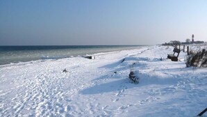 Una spiaggia innevata con un faro in lontananza.