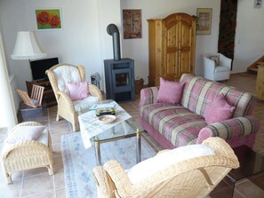 Ein gemütliches Wohnzimmer mit Korbmöbeln, einer Couch, einem Sessel, einem Tisch und einem Kamin.