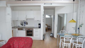 Een compacte woonruimte met een kitchenette, een eethoek en een rode bank met een patroon.