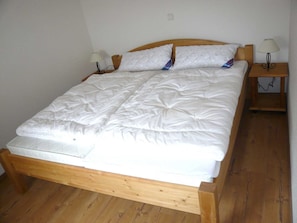 A single-bed room with a wooden frame, white bedding, two bedside lamps, and a small wooden nightstand.