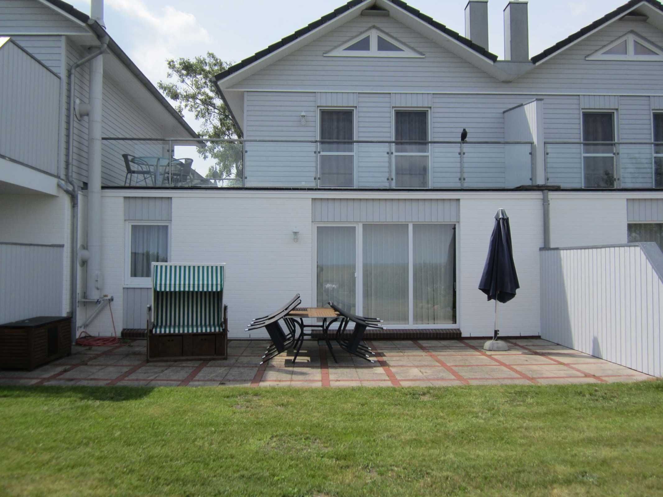 Une maison à deux étages dotée d’un patio comprenant une table et des chaises, un espace salon couvert et une grande porte-fenêtre coulissante.