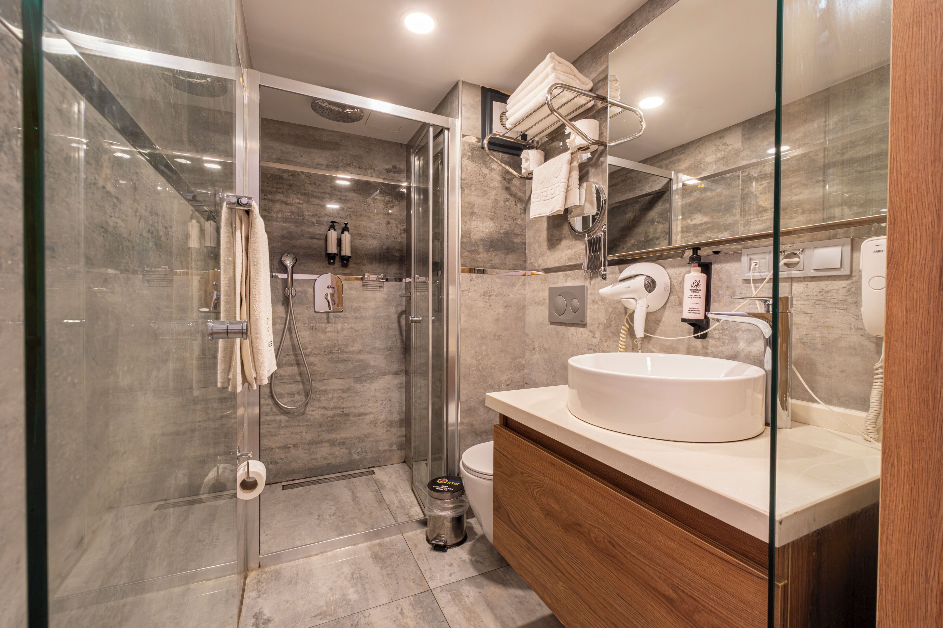 A modern bathroom with a glass-enclosed shower, a white sink, and a wooden vanity.