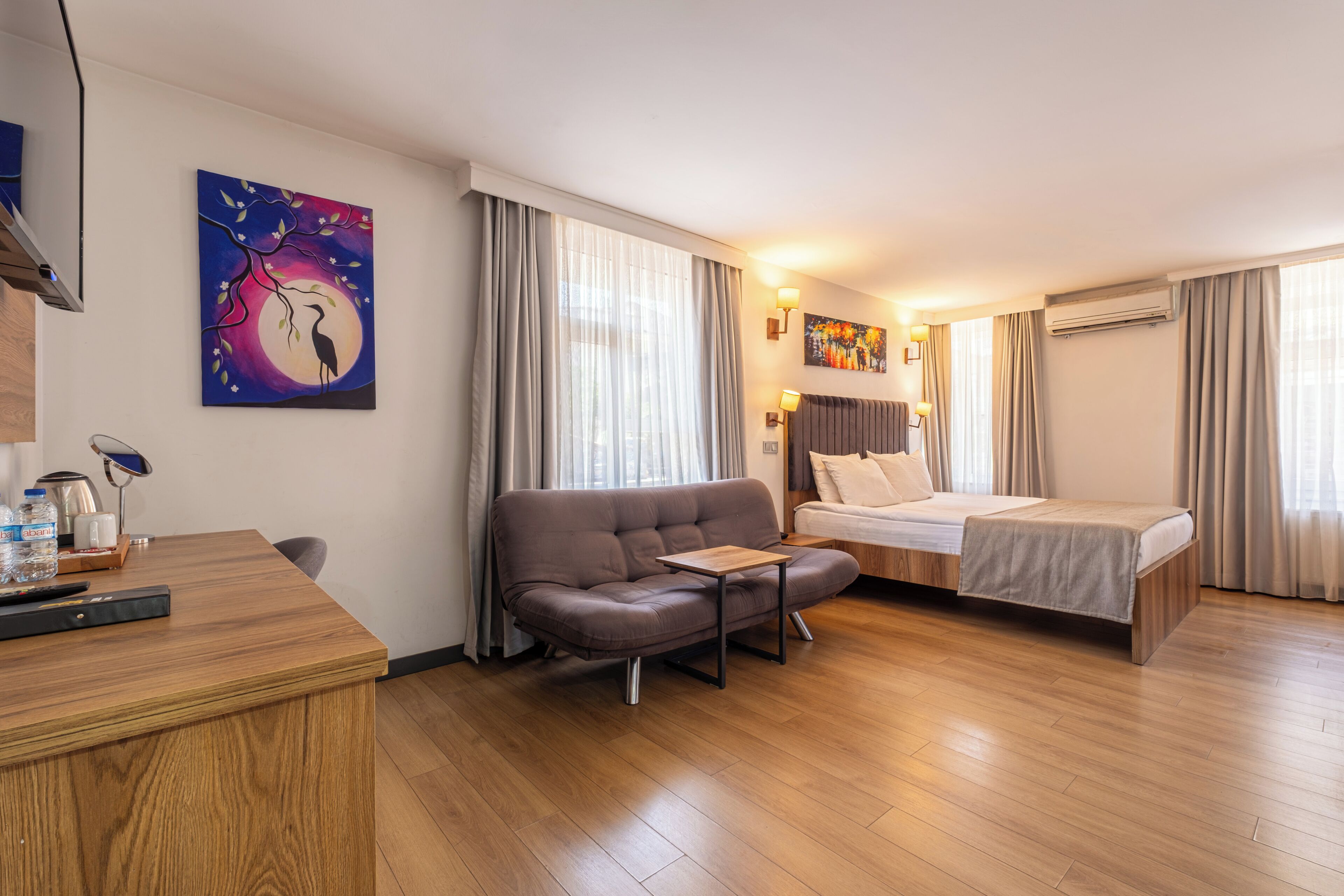A hotel room with a bed, a sofa, a desk, and a painting on the wall.