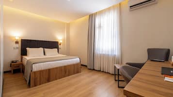 A hotel room with a wooden bed, a desk with a chair, an air conditioner, and a window with curtains.
