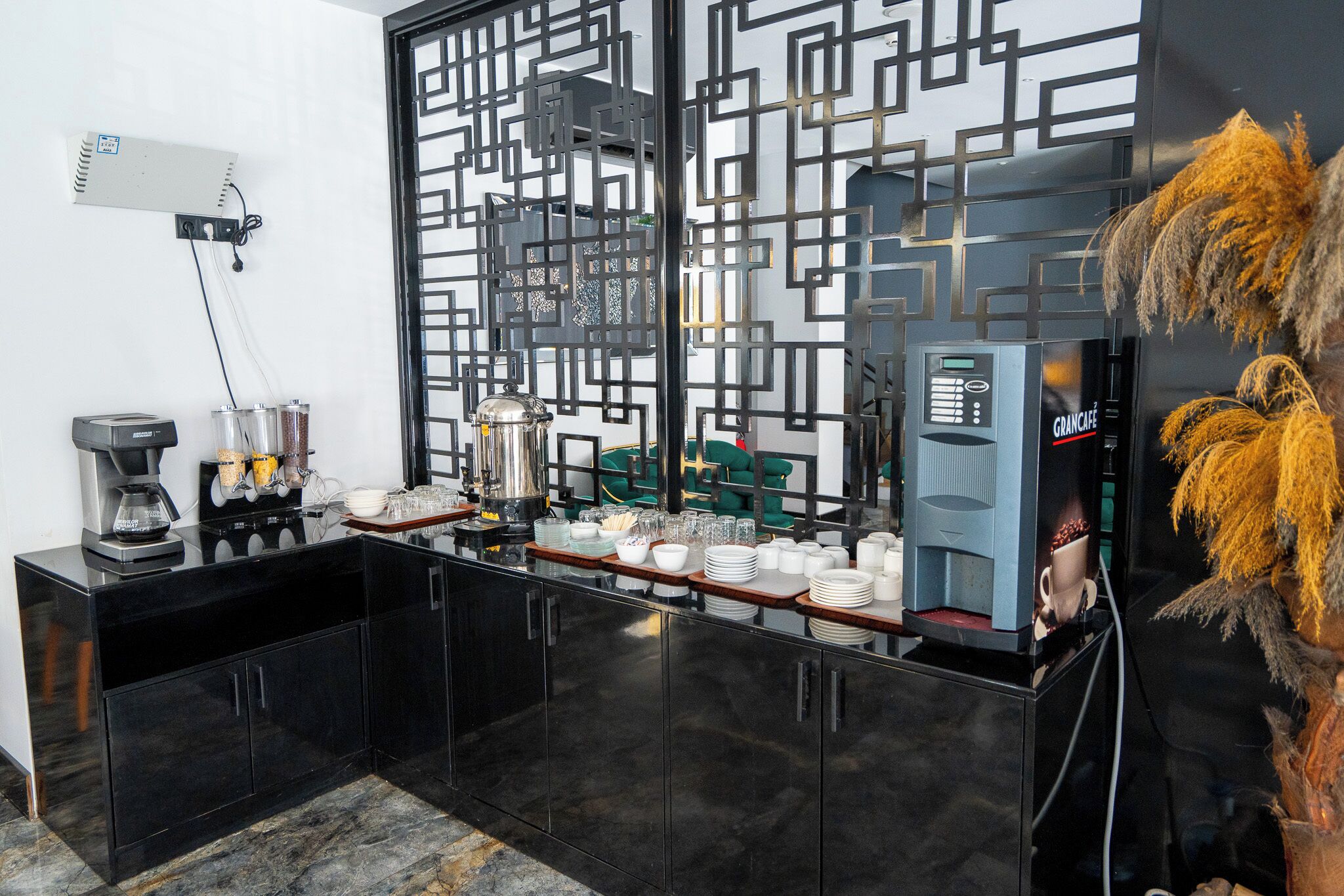 A bar area with a coffee machine, a water dispenser, and a coffee press. There are stacked plates and glasses on the counter.