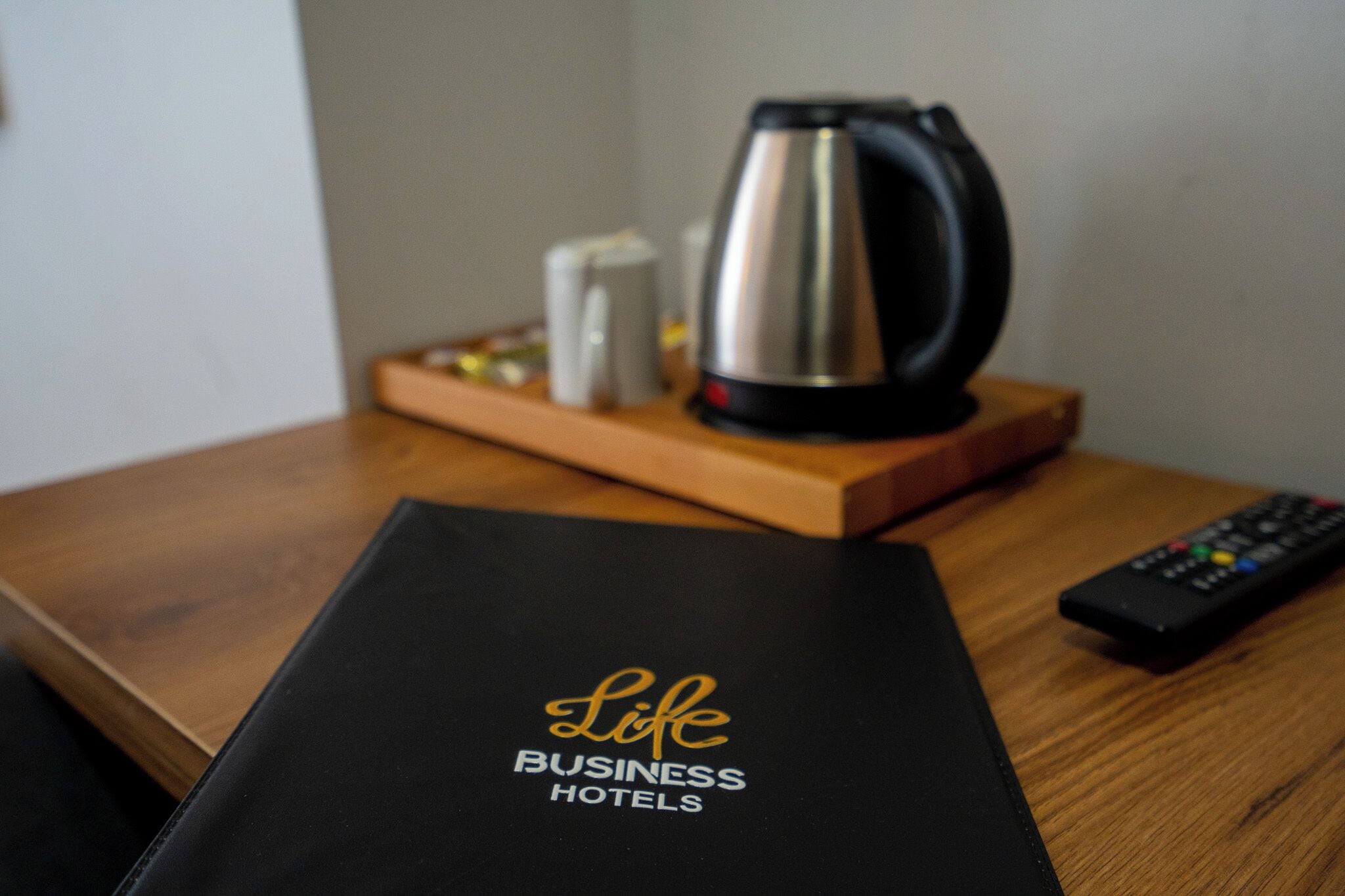 A black folder with 'Life Business Hotels' text, a remote control, and a coffee maker on a wooden table.