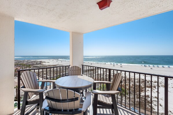 Un balcon avec une table ronde et quatre chaises, donnant sur une plage d’où l’on a une vue dégagée sur l’océan et les personnes qui se promènent sur la plage.