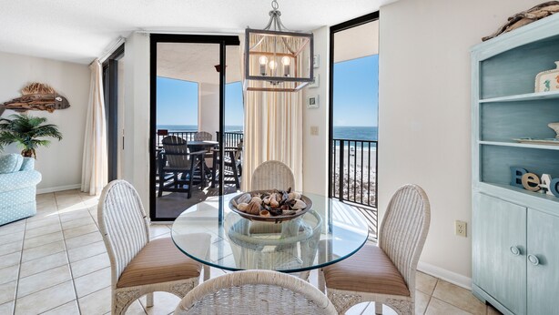 A balcony with a glass table, wicker chairs, and a view of the beach. - Phoenix East 508 | Breathtaking Gulf Views | Family Favorite Condo | My Beach Getaways (Orange Beach)