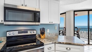 A modern kitchen with a built-in microwave, stove, and white cabinetry. A knife block is visible on the counter. - Phoenix East 508 | Breathtaking Gulf Views | Family Favorite Condo | My Beach Getaways (Orange Beach)
