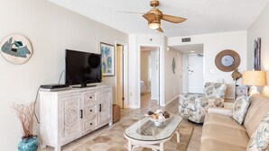 A living room with a TV, white cabinet, glass coffee table, beige sofa, and patterned armchairs. - Phoenix East 508 | Breathtaking Gulf Views | Family Favorite Condo | My Beach Getaways (Orange Beach)