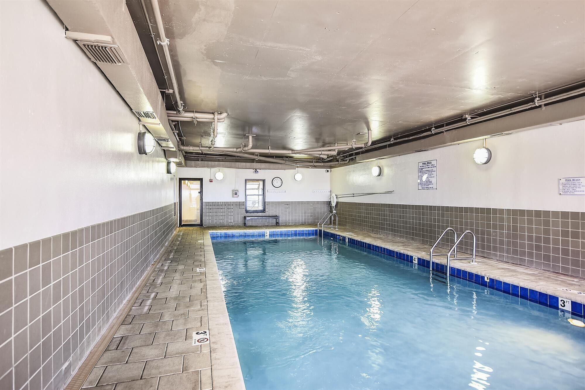 An indoor swimming pool with tiled walls and a tiled floor, equipped with a starting block and a ladder.