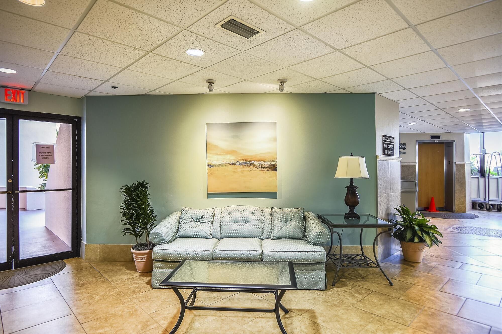 A lobby with a sofa, a coffee table, a lamp, and a painting on the wall.
